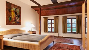 Una habitación con una cama de mimbre, un cuadro abstracto grande, una ventana con cortinas y una alfombra estampada.
