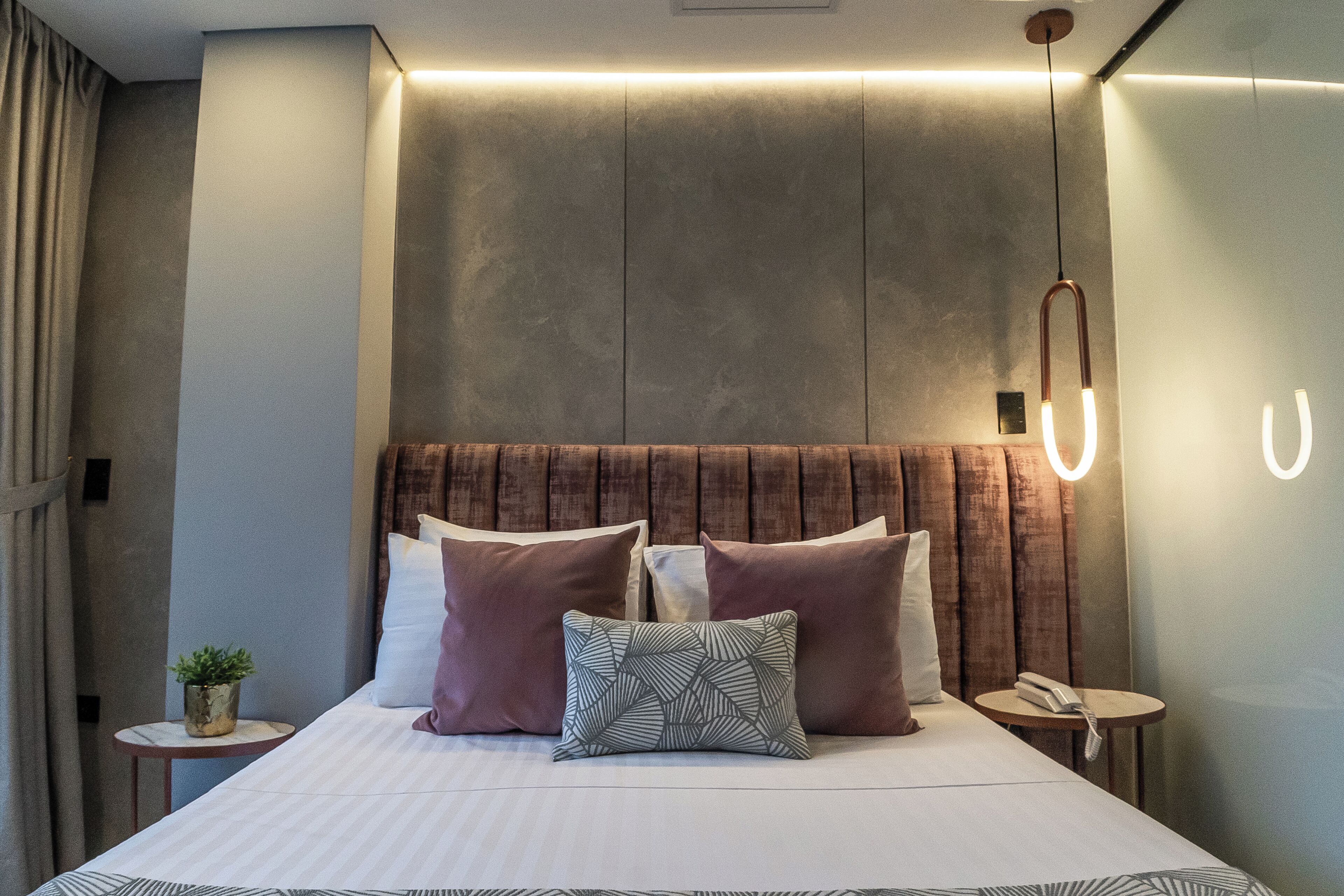 A modern hotel room with a large bed, a bedside table with a phone, and a small potted plant.