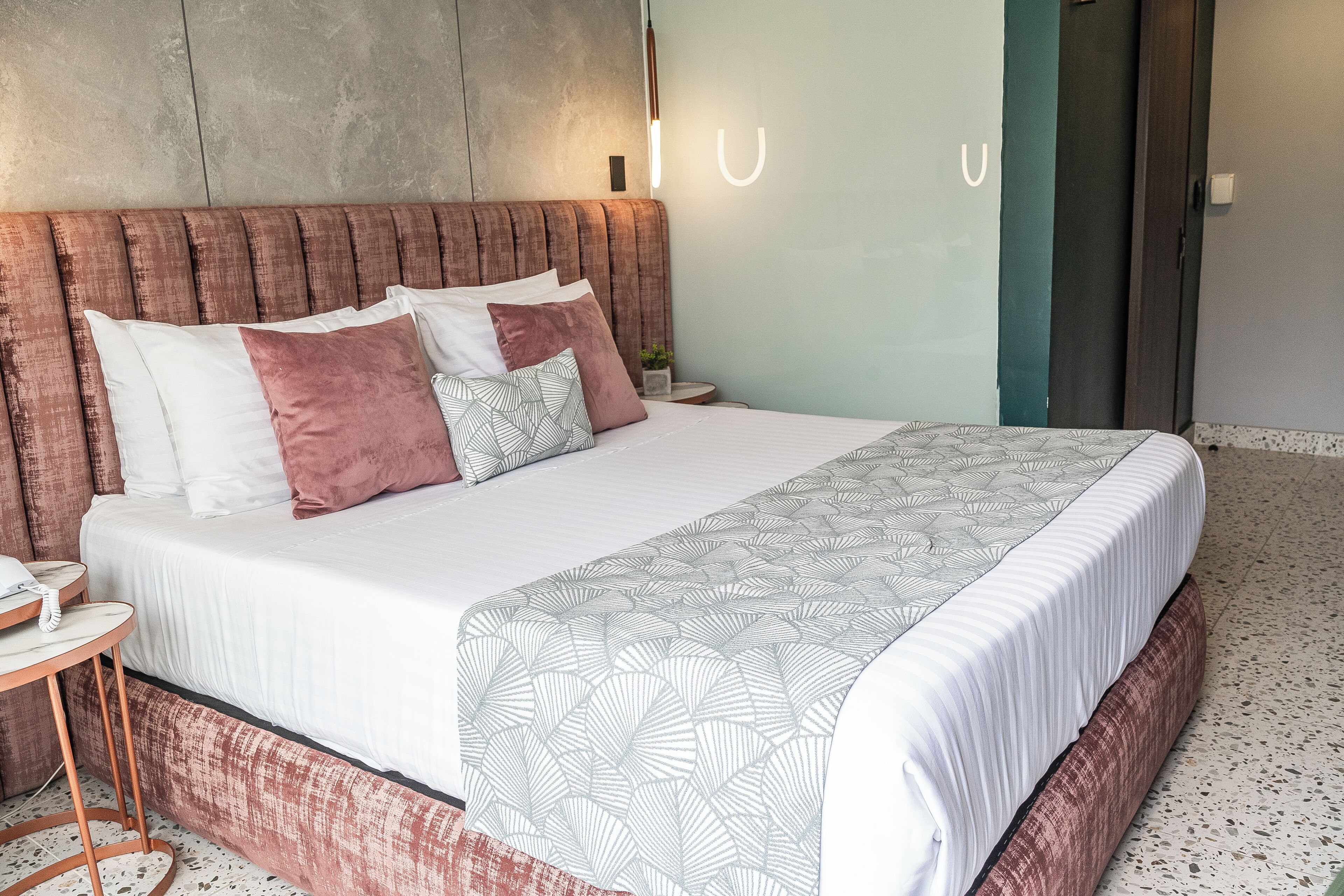 A neatly made bed with a patterned bedspread, a headboard with a textured design, and a bedside table with a lamp.