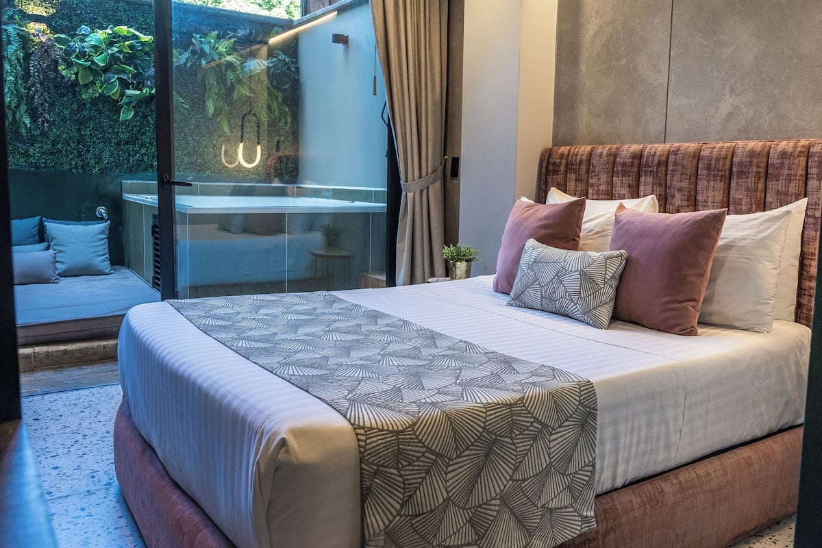 Quarto moderno com cama grande, porta de vidro que dá para uma varanda e vista para o verde lá fora.