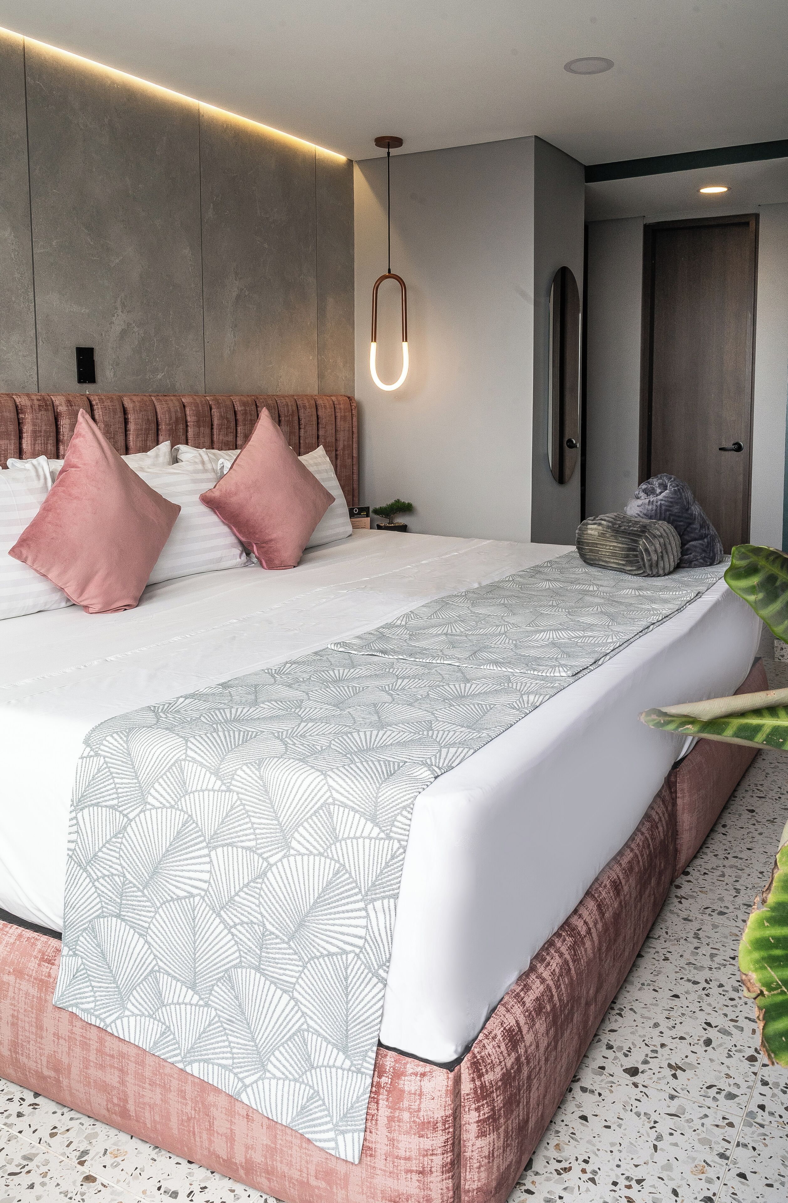 Un dormitorio moderno con una cama grande, almohadas rosa y blancas, una colcha estampada y una lámpara colgante.