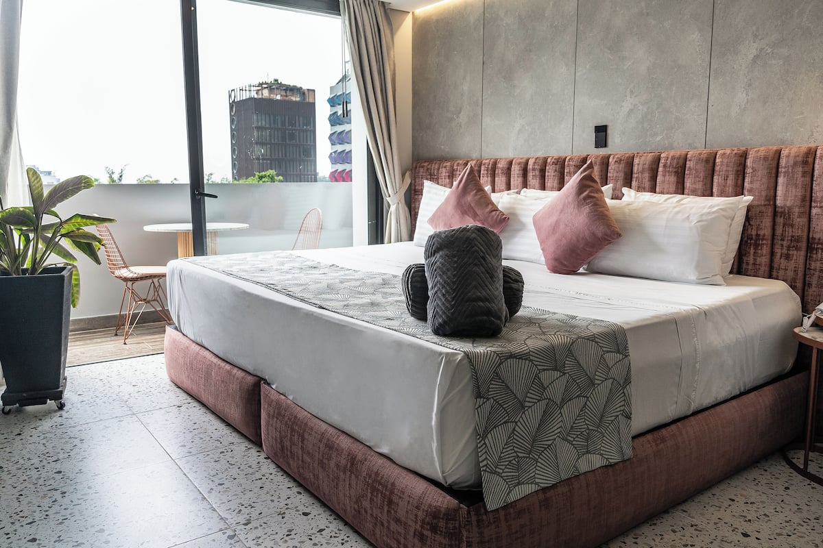 Quarto moderno com uma cama grande, uma planta em vaso e vista da cidade.