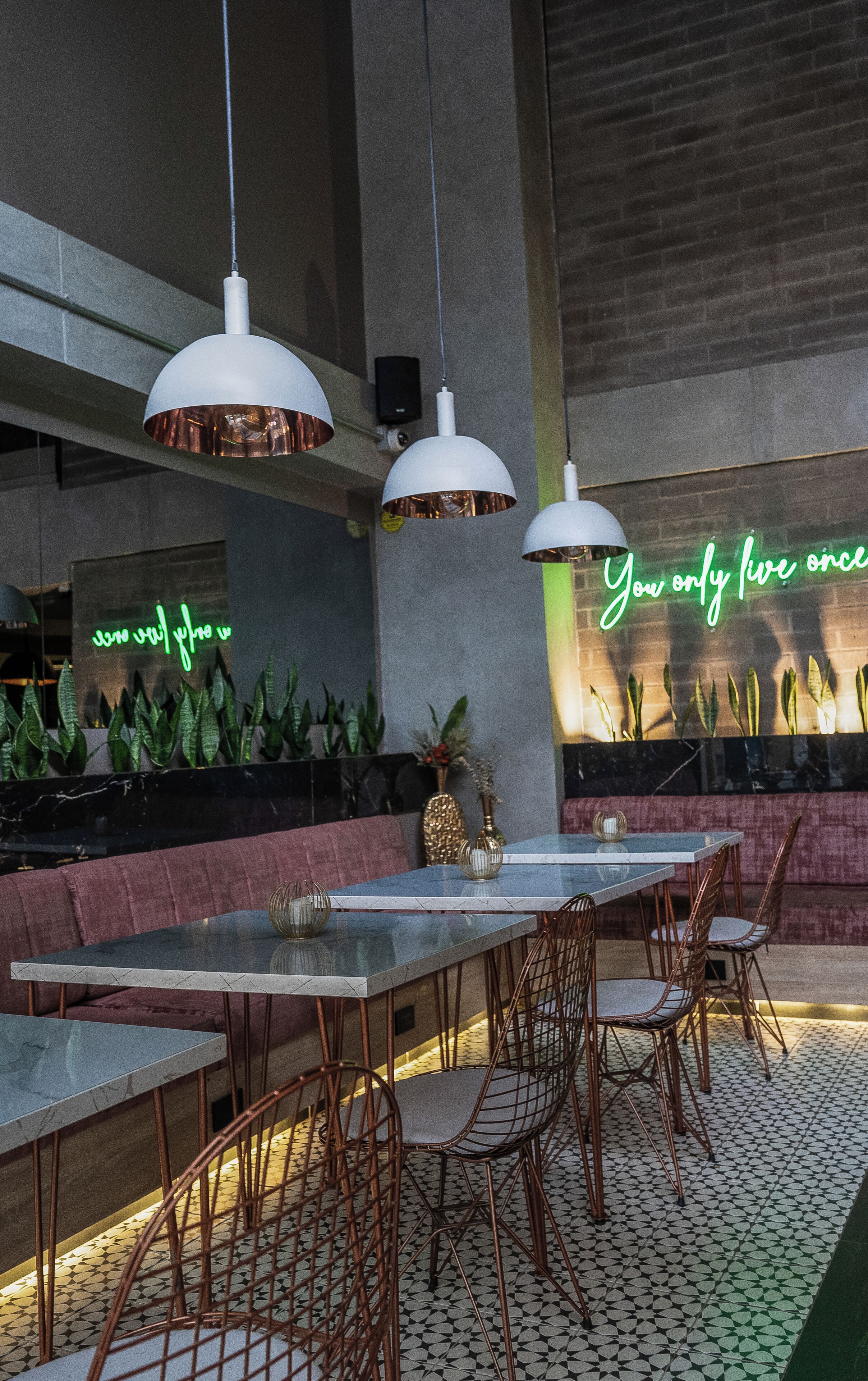 A modern indoor dining area with a long table, multiple chairs, and hanging pendant lights.