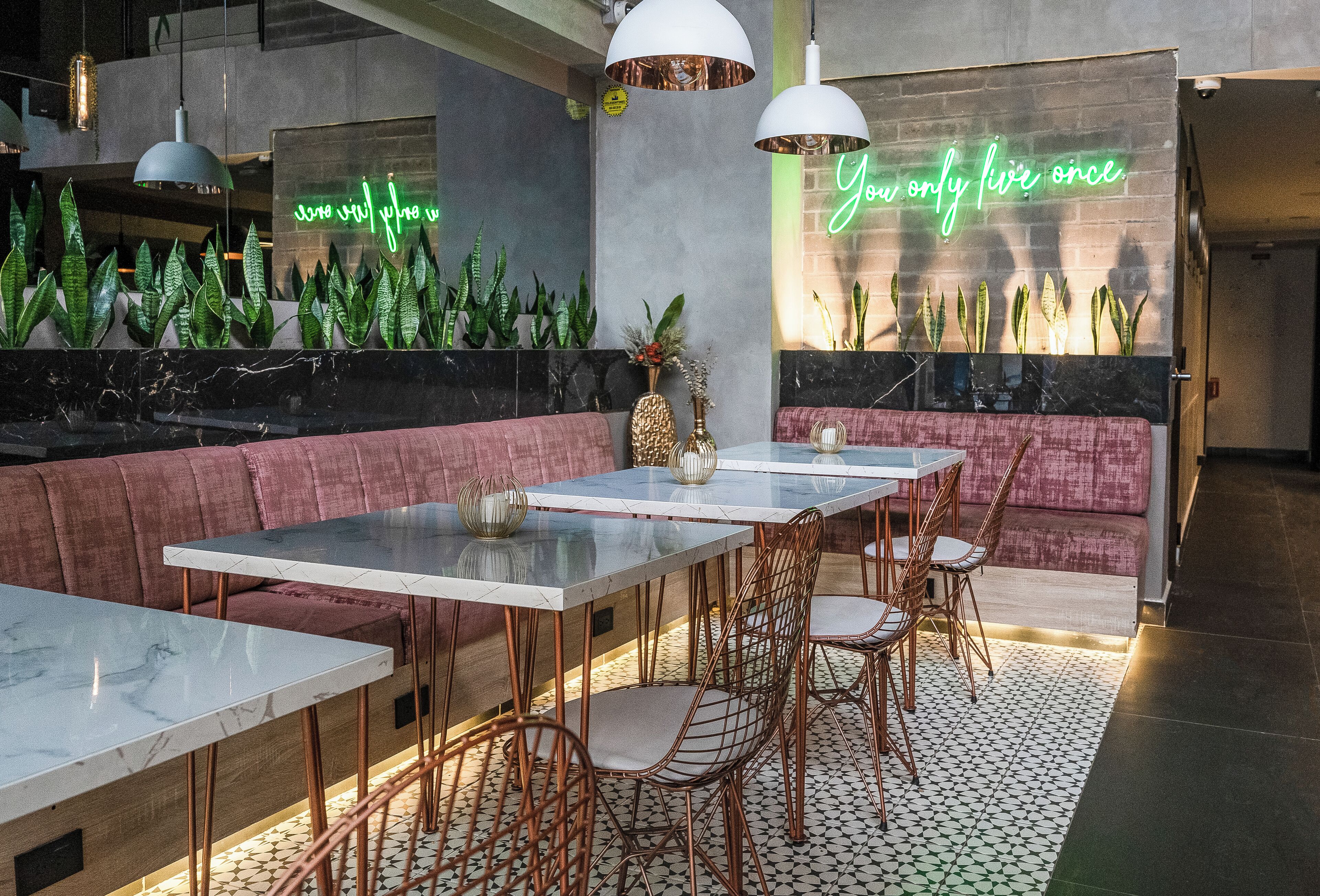 A modern restaurant interior with marble tables, cushioned seating, and a neon sign.