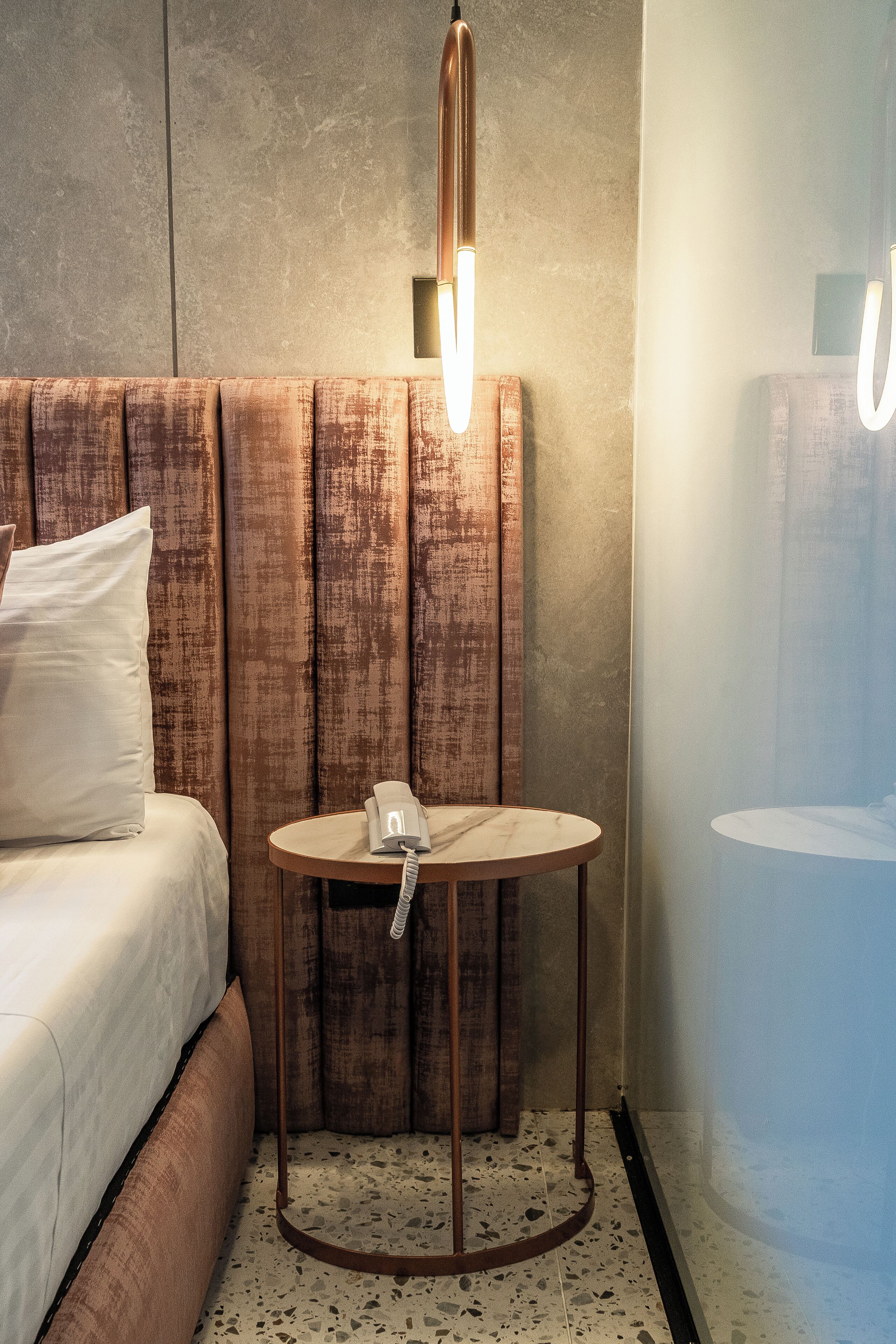 Habitación de hotel con cama, una mesa redonda con teléfono y una lámpara fijada a la pared.