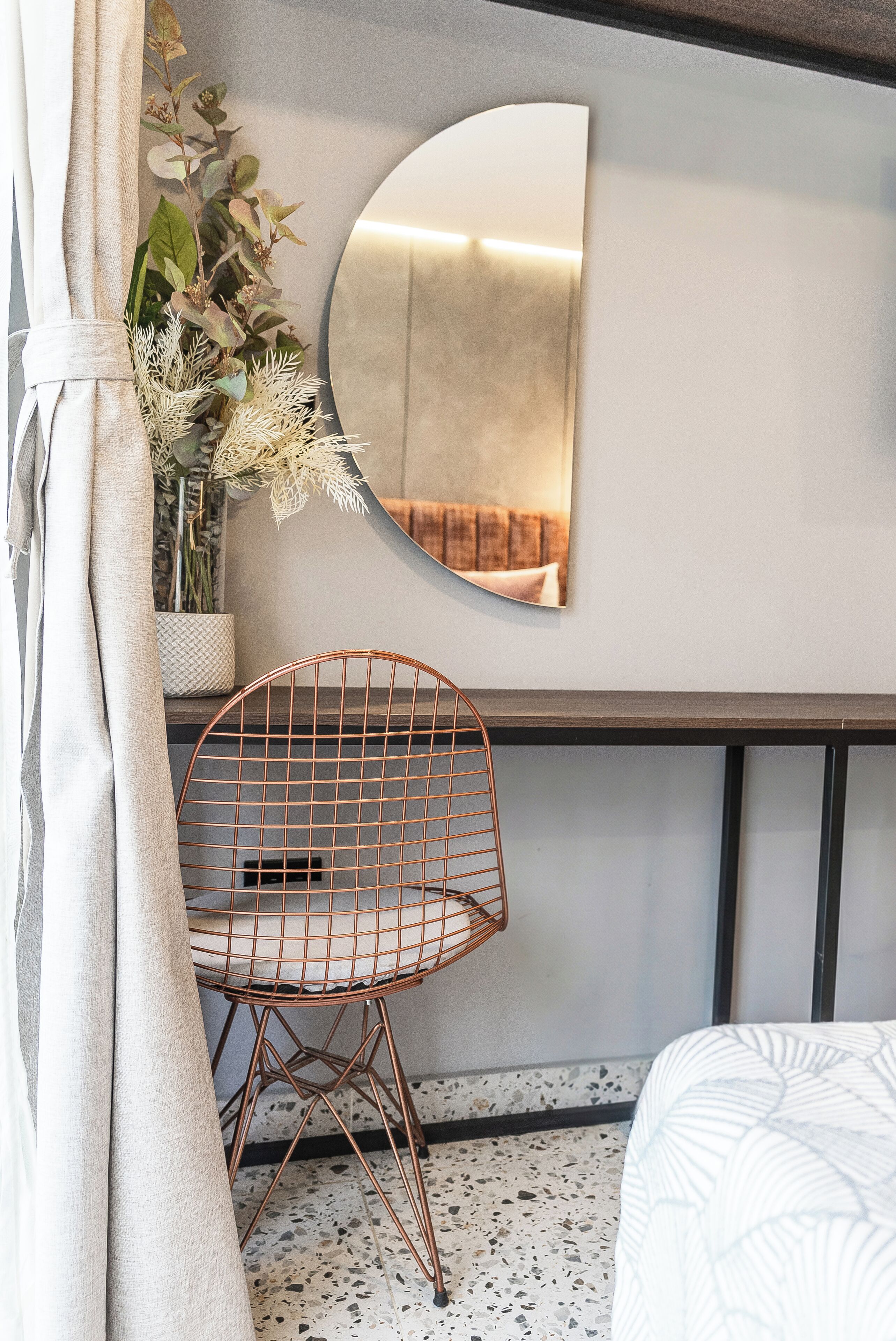 Une chambre à coucher moderne avec un miroir rond, une chaise en fil de fer et un lit.