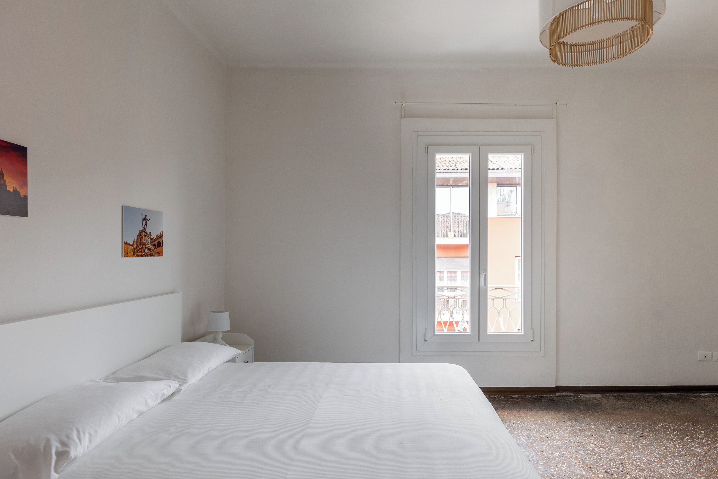 A bedroom with a bed, a nightstand, a window, and a wall-mounted lamp.