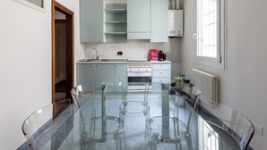 A modern kitchen with a glass dining table, white cabinets, and a built-in oven. - Alessandrini Apartment alla Finestrella by Wonderful Italy (Bologna)