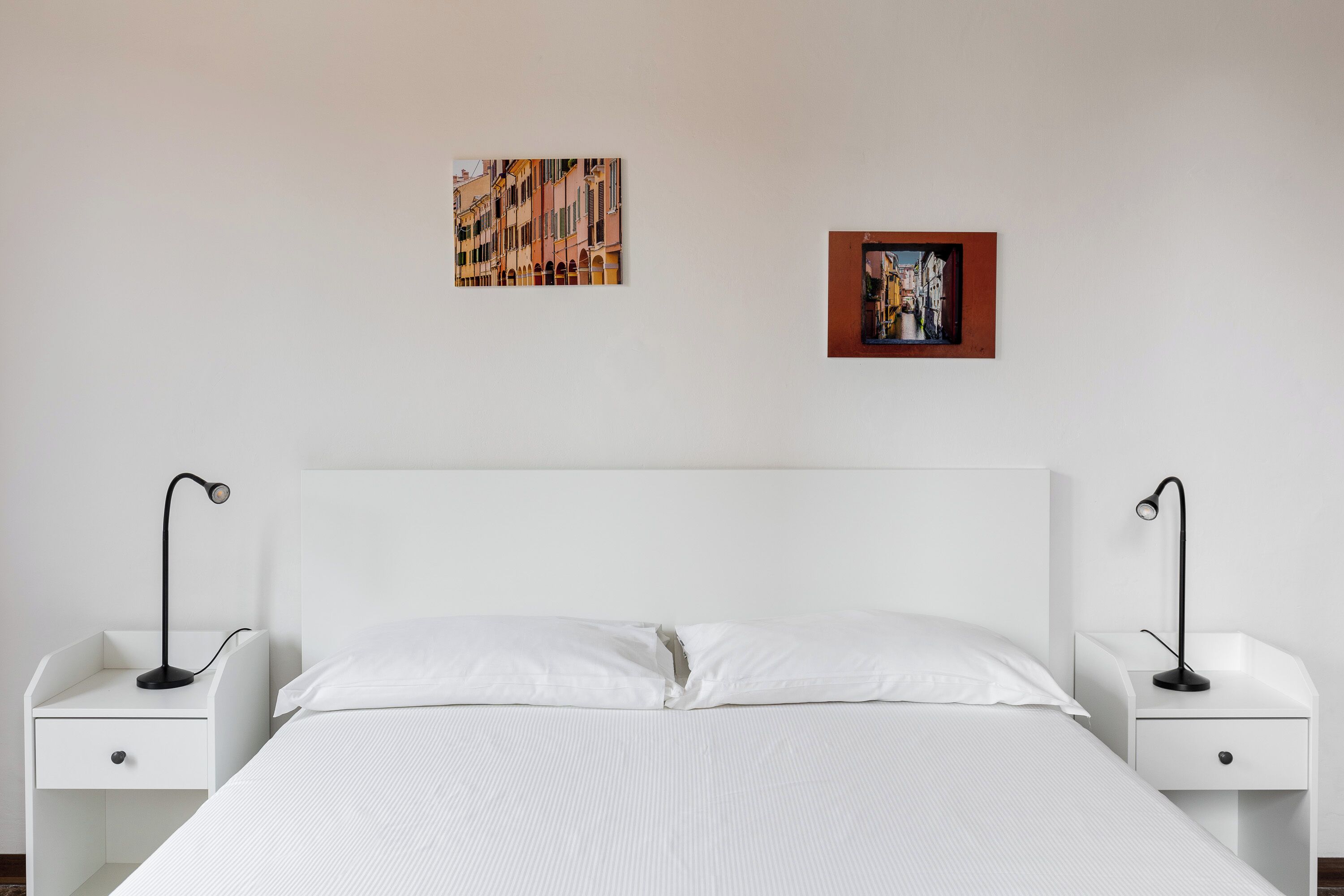 A minimalist hotel room with a large bed, two bedside tables, and two wall-mounted lamps.