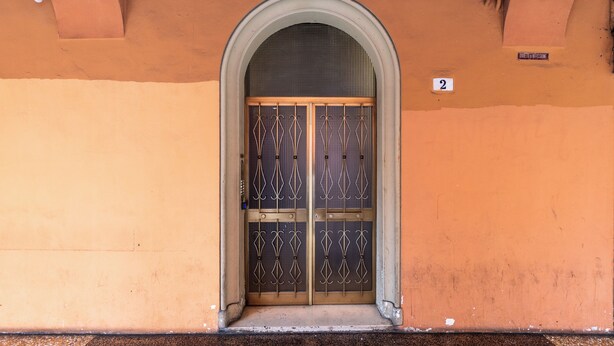 A building entrance with a large arched doorway, a number '2' sign, and a metal gate. - Alessandrini Apartment alla Finestrella by Wonderful Italy (Bologna)