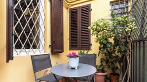 A small outdoor patio with a round table and two chairs, surrounded by potted plants and a yellow wall. - Alessandrini Apartment alla Finestrella by Wonderful Italy (Bologna)