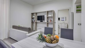 A modern living room with a dining table, a sofa, and a TV mounted on a wooden shelf. - Tourist Apartment Civitavecchia (Civitavecchia)