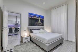 A modern bedroom with a large bed, a nightstand, a painting of a cityscape, and a view of a dining area. - Tourist Apartment Civitavecchia (Civitavecchia)