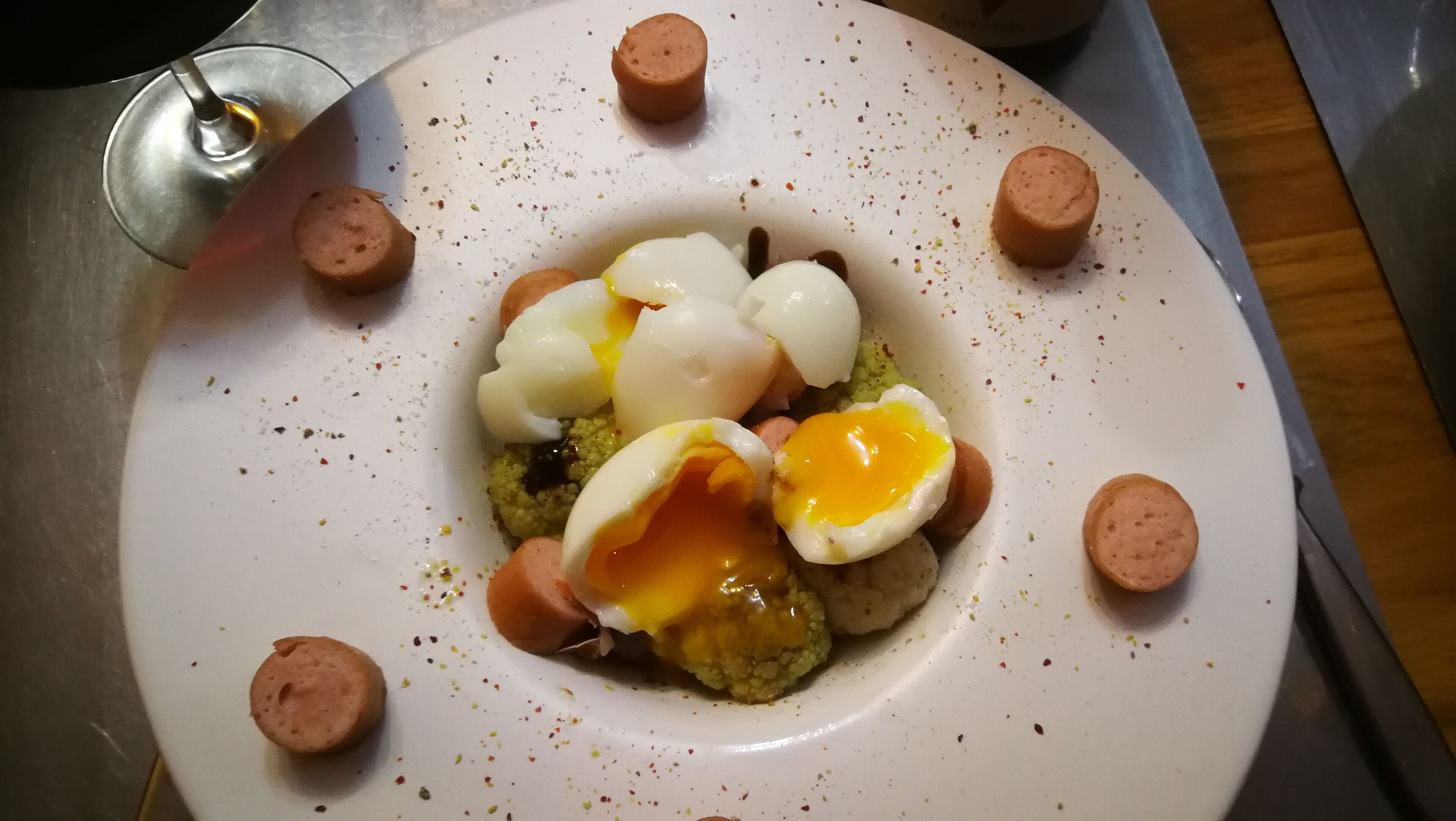 Une assiette contenant un plat composé de tranches de saucisse, d’œufs durs et d’une garniture verte.