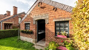 A brick house with a pitched roof, a visible chimney, and a small garden with potted plants.