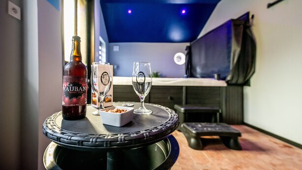 A bar area with a bottle of La Vauban Barley Style beer, two glasses, and a small bowl of snacks on a round table.