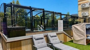 Eine Dachterrasse mit Glasfassaden, Liegestühlen und einem Poolbereich.