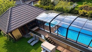 Ein modernes Haus mit einem überdachten Pool, einer Terrasse mit Sitzgelegenheiten und einer überdachten Deckfläche.