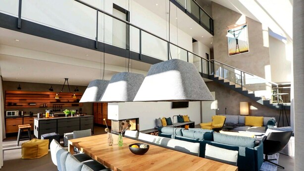 A spacious living area with a wooden dining table, grey sofas, and a staircase leading to an upper level.