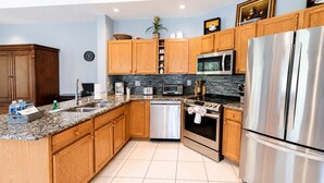 A modern kitchen with wooden cabinets, stainless steel appliances, a granite countertop, and a tiled backsplash.