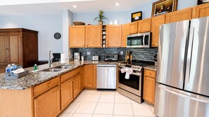 Una cocina moderna con armarios de madera, electrodomésticos de acero inoxidable, encimera de granito y salpicadero de azulejos.
