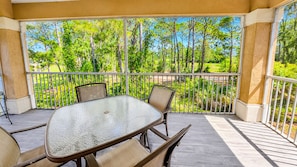 A covered outdoor patio with a glass table and chairs, surrounded by metal railings and a view of trees. - Right Direction Rentals 1 Bedroom Villa 8954 (Port St. Lucie)