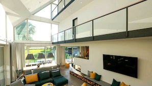 A spacious living area with a high ceiling, large windows, and a modern design.