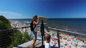 Un balcón con vistas a una playa concurrida, sombrillas y gente.