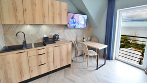 A modern kitchen with wooden cabinets, a black countertop, and a built-in TV. There is a dining area with a table and chairs, and a balcony with a view of the sea. - Comfortable apartment with a sea view (Ustronie Morskie)
