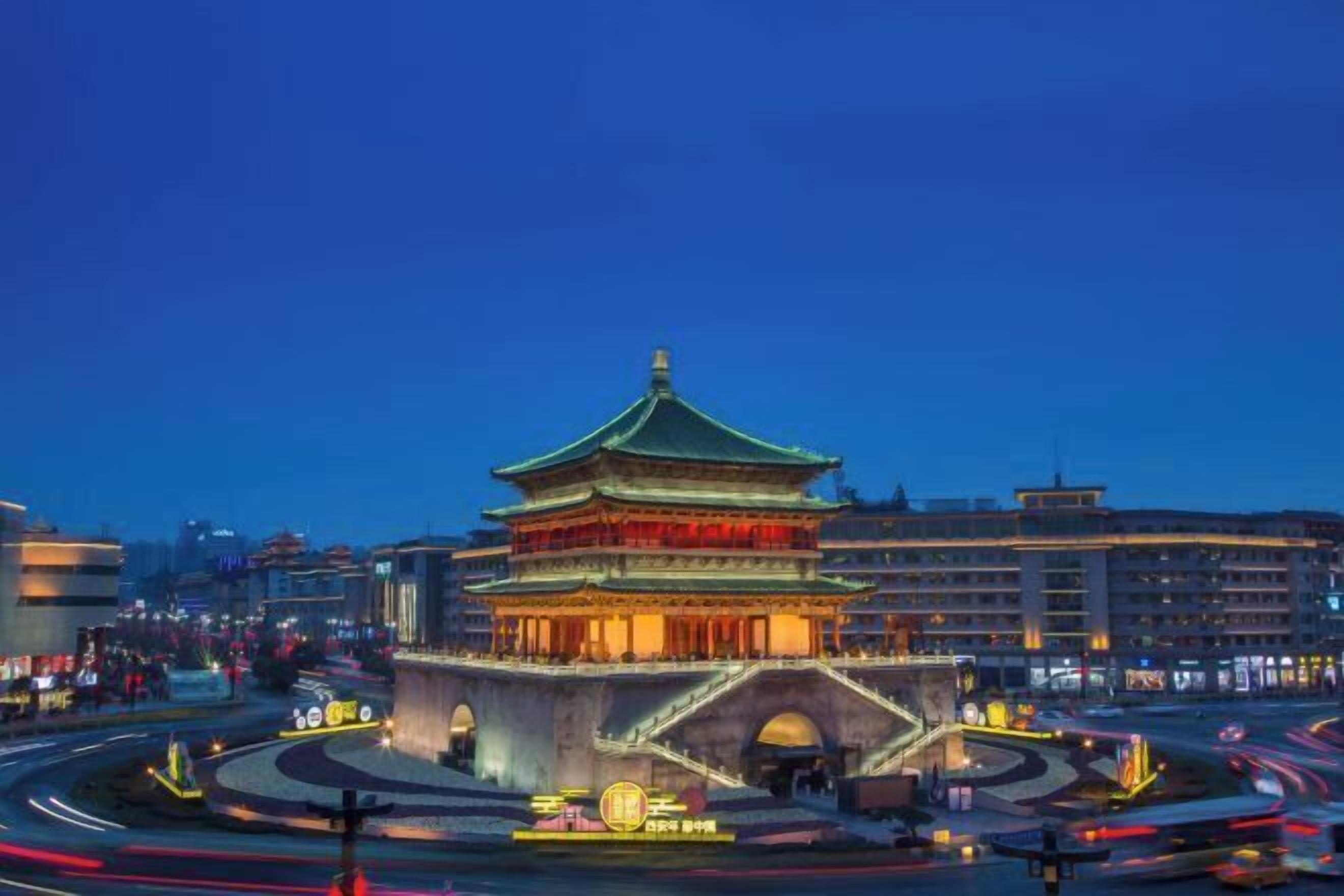 A traditional multi-tiered building with a green roof, surrounded by a modern urban environment with roads and buildings.