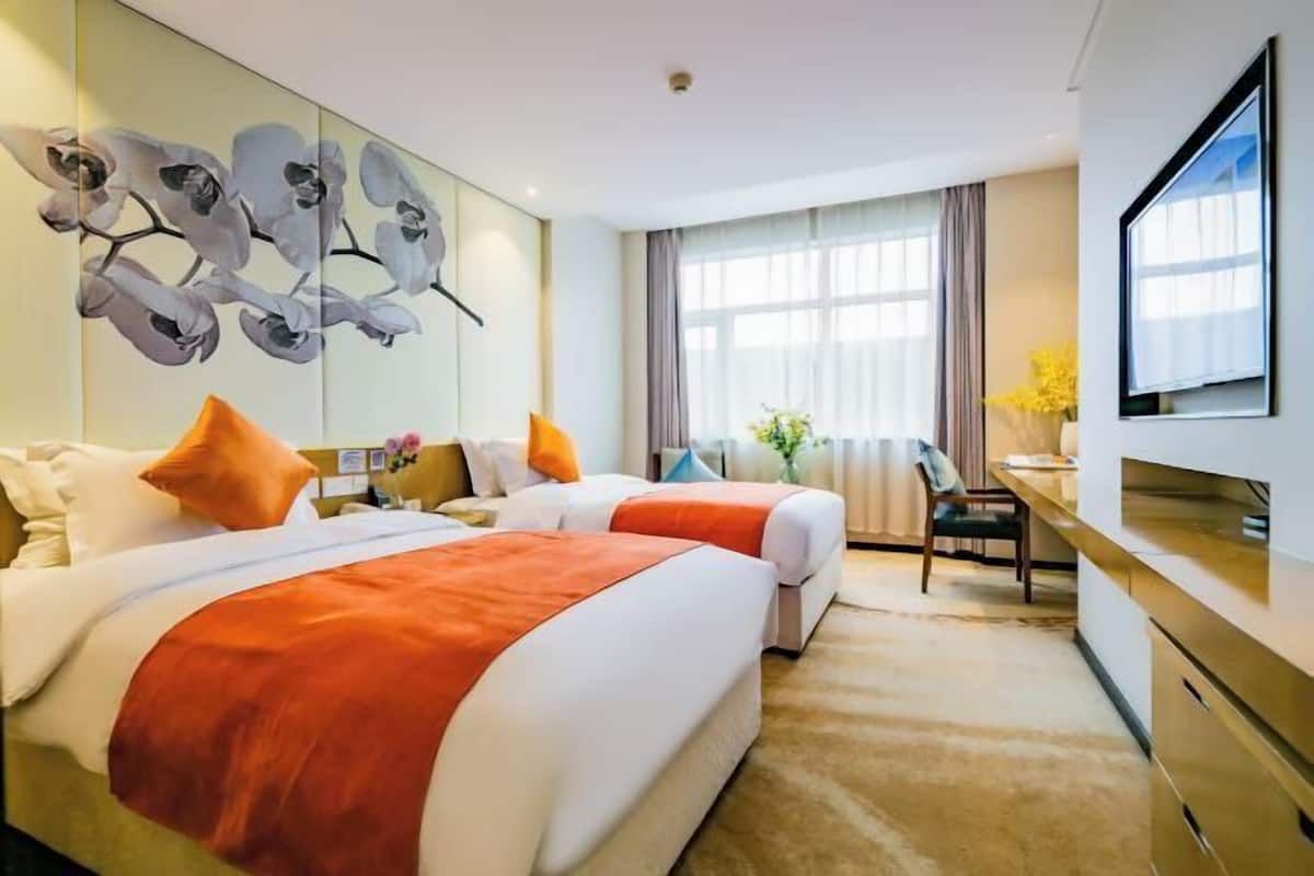 Une chambre d’hôtel avec deux lits, un bureau, une chaise, une télévision et une grande fenêtre avec des rideaux.