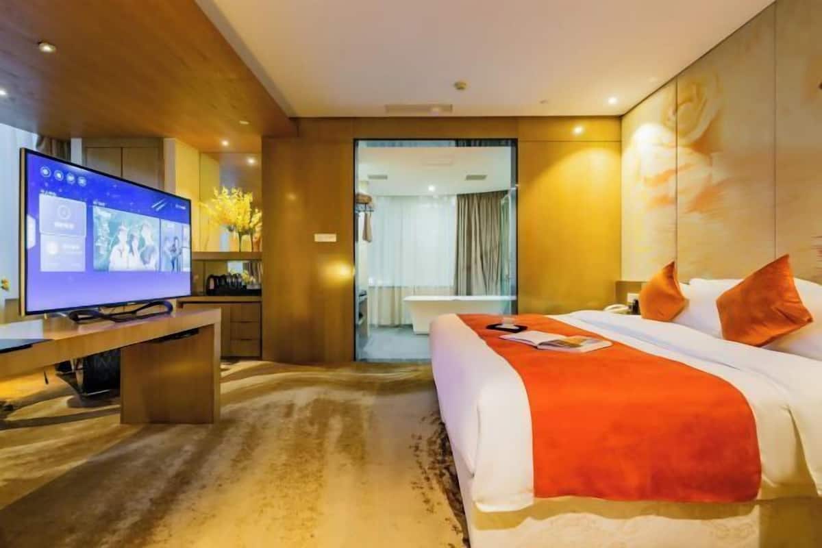 Une chambre d’hôtel dotée d’une grande télévision à écran plat, d’un lit recouvert d’une courtepointe orange, d’un bureau avec un ordinateur et donnant sur le couloir.