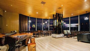 Una habitación amplia con techo de madera, una mesa de billar y una zona de estar con sillas y sofá.