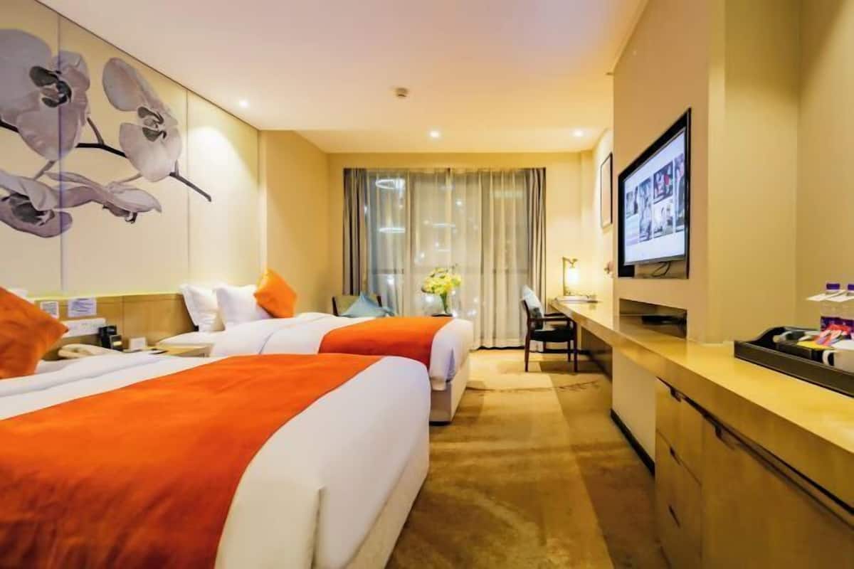Une chambre d’hôtel avec deux lits, un bureau, une télévision et une grande fenêtre avec des rideaux.