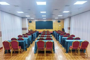 A conference room with rows of tables and chairs, a stage with a screen, and a wooden floor. - Xi'an Peace Arch Hotel (Xi'an)