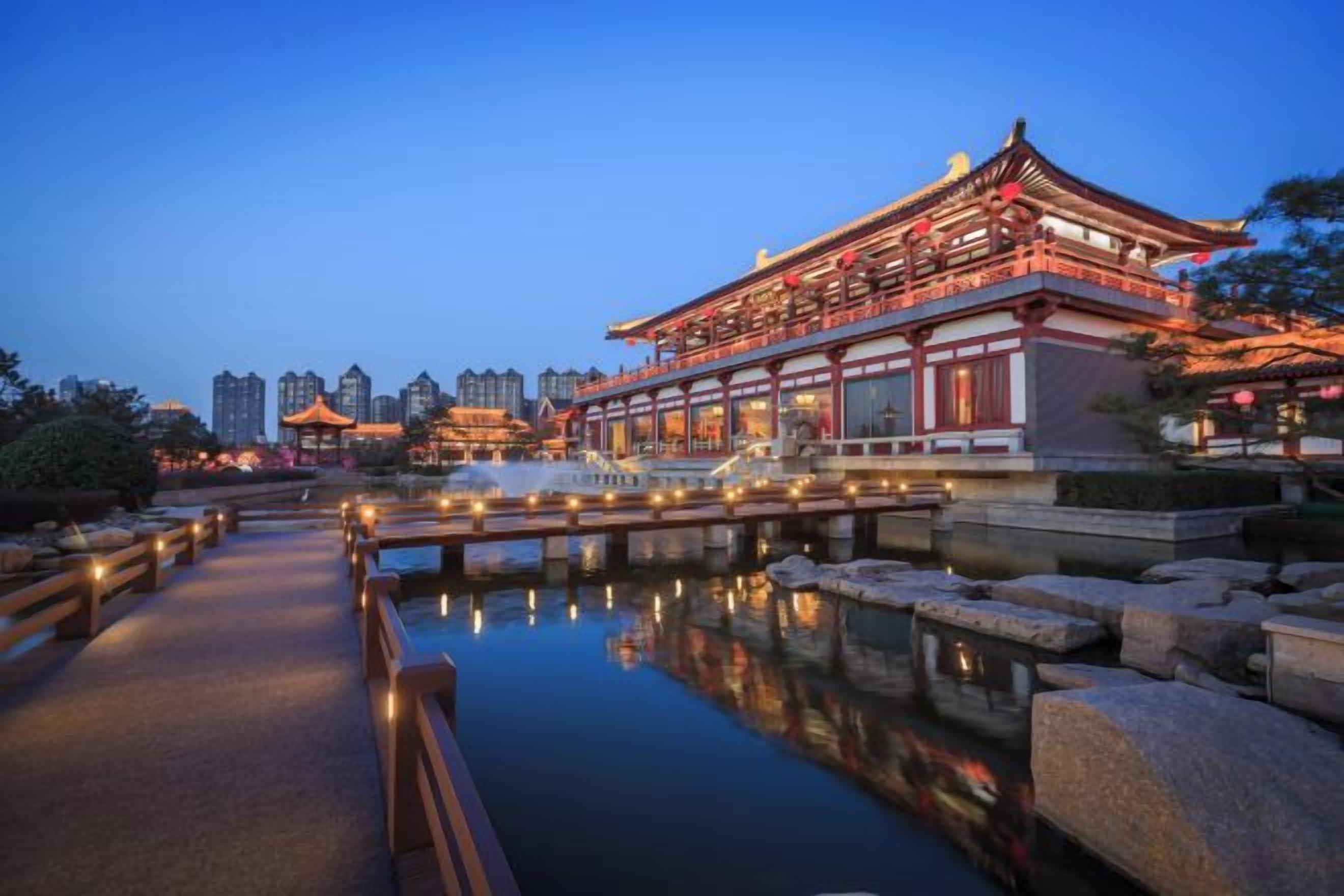 A traditional building with a reflection in the water, surrounded by a stone pathway and a wooden bridge.