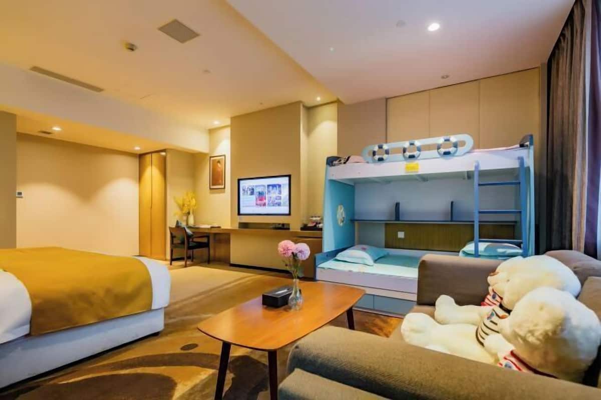 Une chambre d’hôtel équipée d’un lit superposé, d’un canapé, d’un bureau avec un ordinateur et d’une télévision.