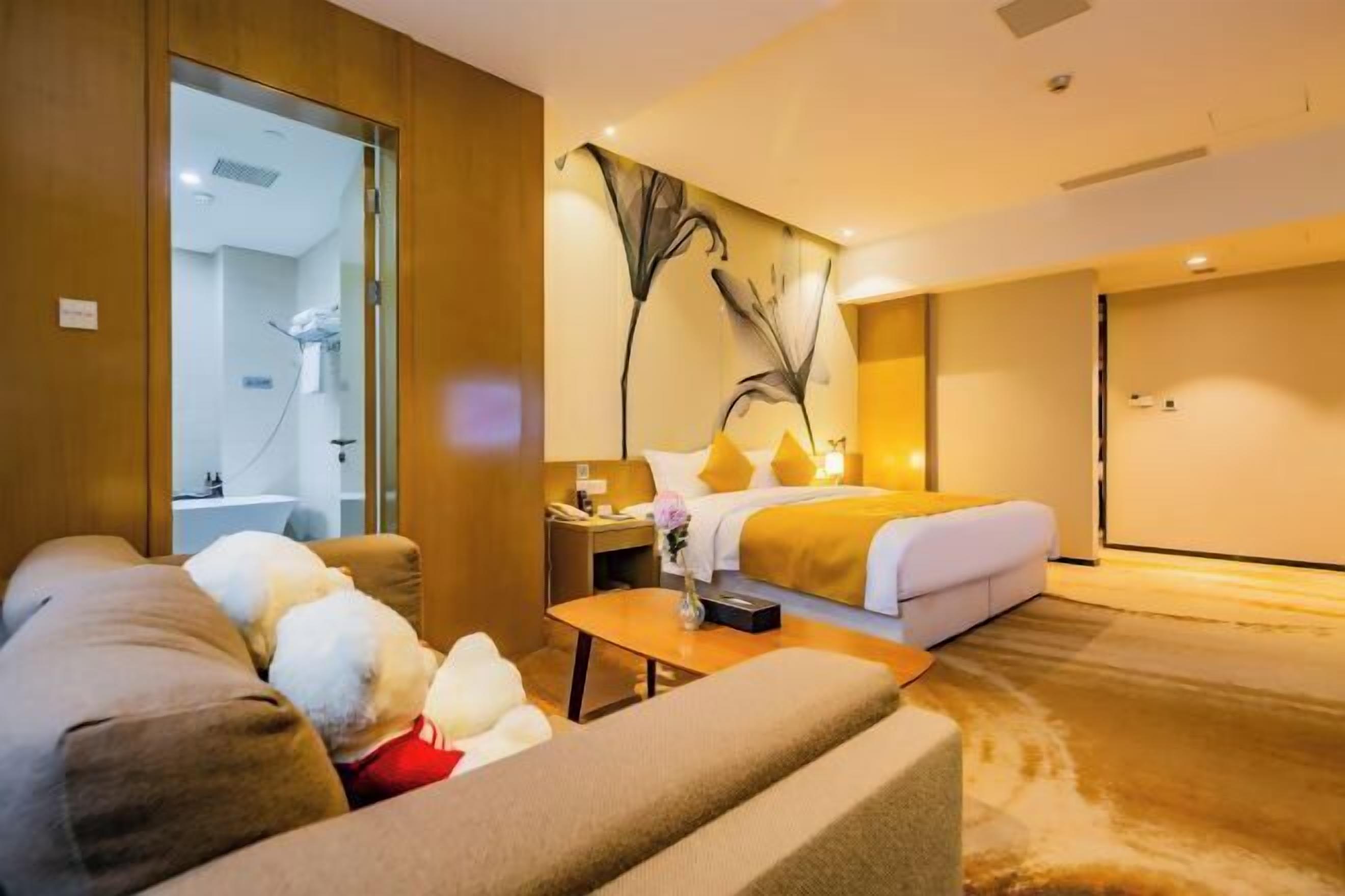 Une chambre d’hôtel comprenant un lit, un canapé, une table basse, une table de chevet et une salle de bain visible à travers une porte en verre.