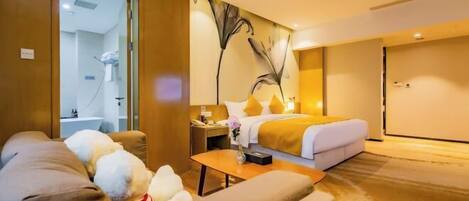 Une chambre d’hôtel comprenant un lit, un canapé, une table basse, une table de chevet et une salle de bain visible à travers une porte en verre.