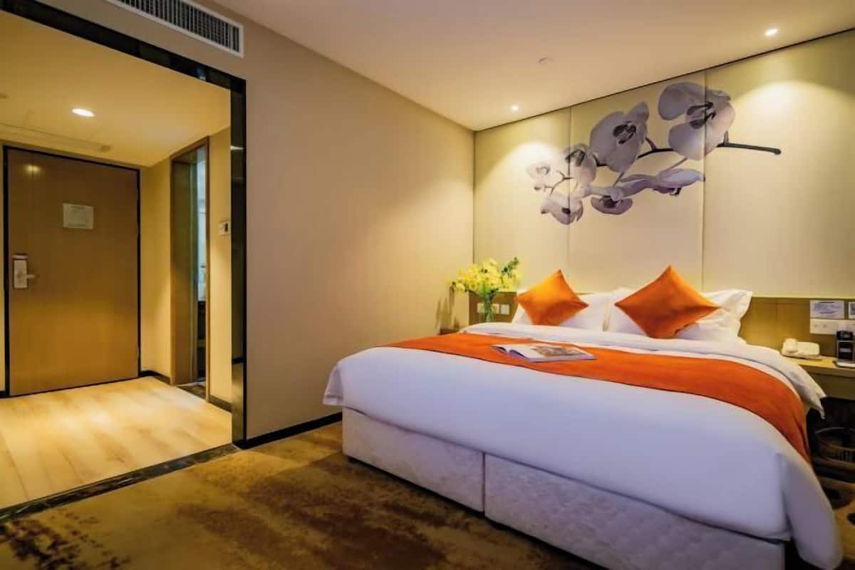 Une chambre d’hôtel avec un grand lit, une table de chevet, un vase de fleurs et un tableau représentant une orchidée accroché au mur.