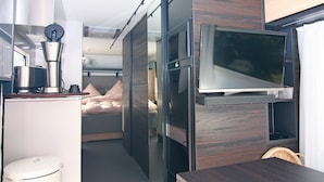A compact room with a bed, a small kitchenette, a TV, and a dining area. - Dreamer Luxus-Caravan am Achterwasser, Lütow (Lütow)