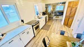 A compact kitchen with white cabinets, a stove, and a dining area with a wooden table and chairs. - Cascade Basecamp: close to fun! (Cascade)