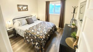 A bedroom with a bed, a nightstand, a dresser, a world map artwork, a window with curtains, and a coat rack. - Cascade Basecamp: close to fun! (Cascade)