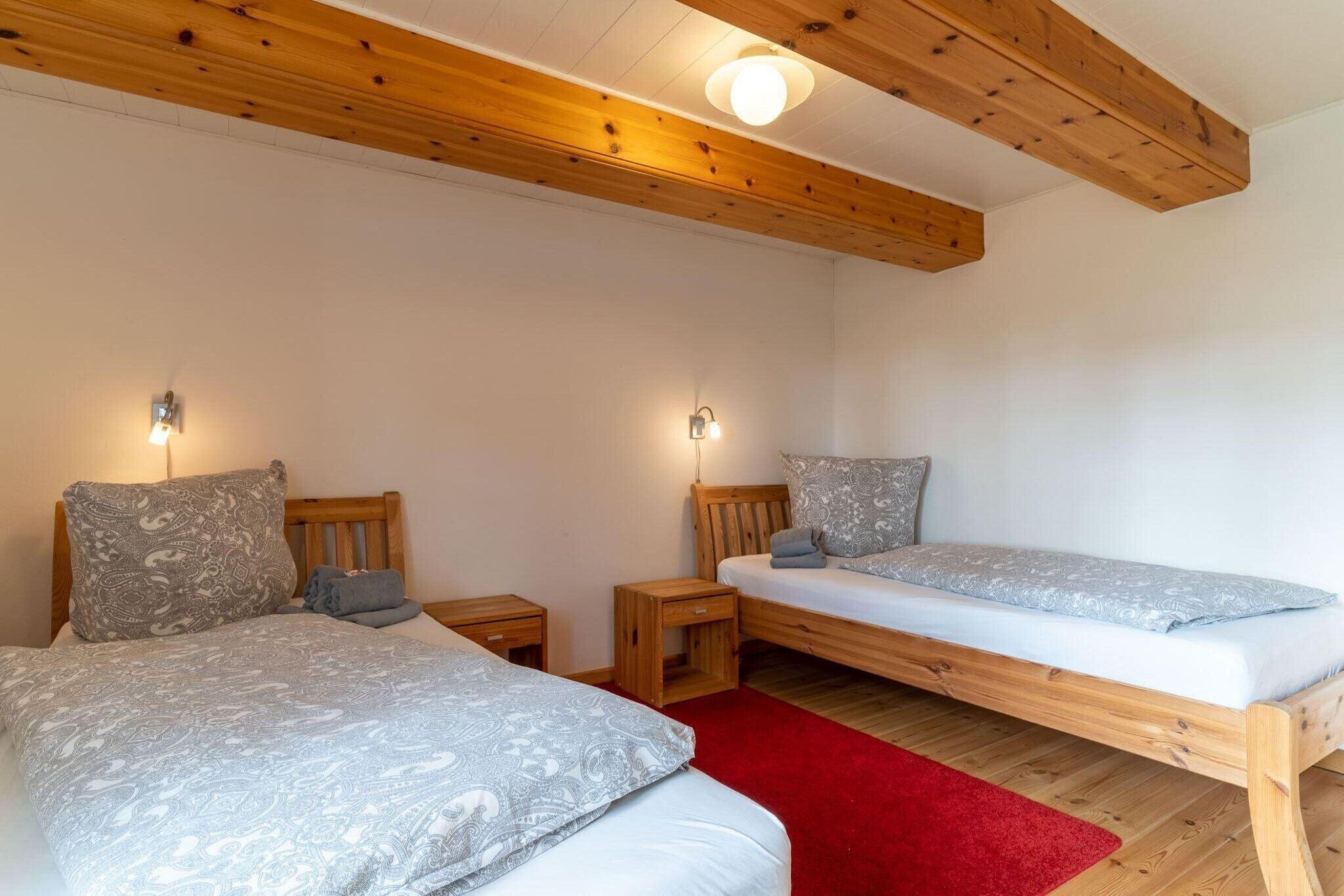 Quarto com duas camas, cabeceiras de madeira, mesas de cabeceira e tapete vermelho.