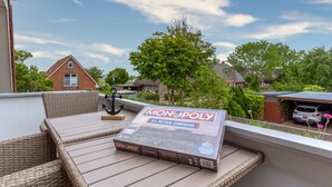 A Monopoly board game on a wicker table on a balcony with a view of houses and trees. - Wohnung in St.Peter Ording (St.Peter Ording)