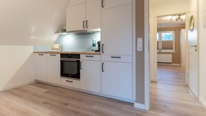 A modern kitchen with white cabinets, a built-in oven, and a countertop with a kettle. - Wohnung in St.Peter Ording (St.Peter Ording)