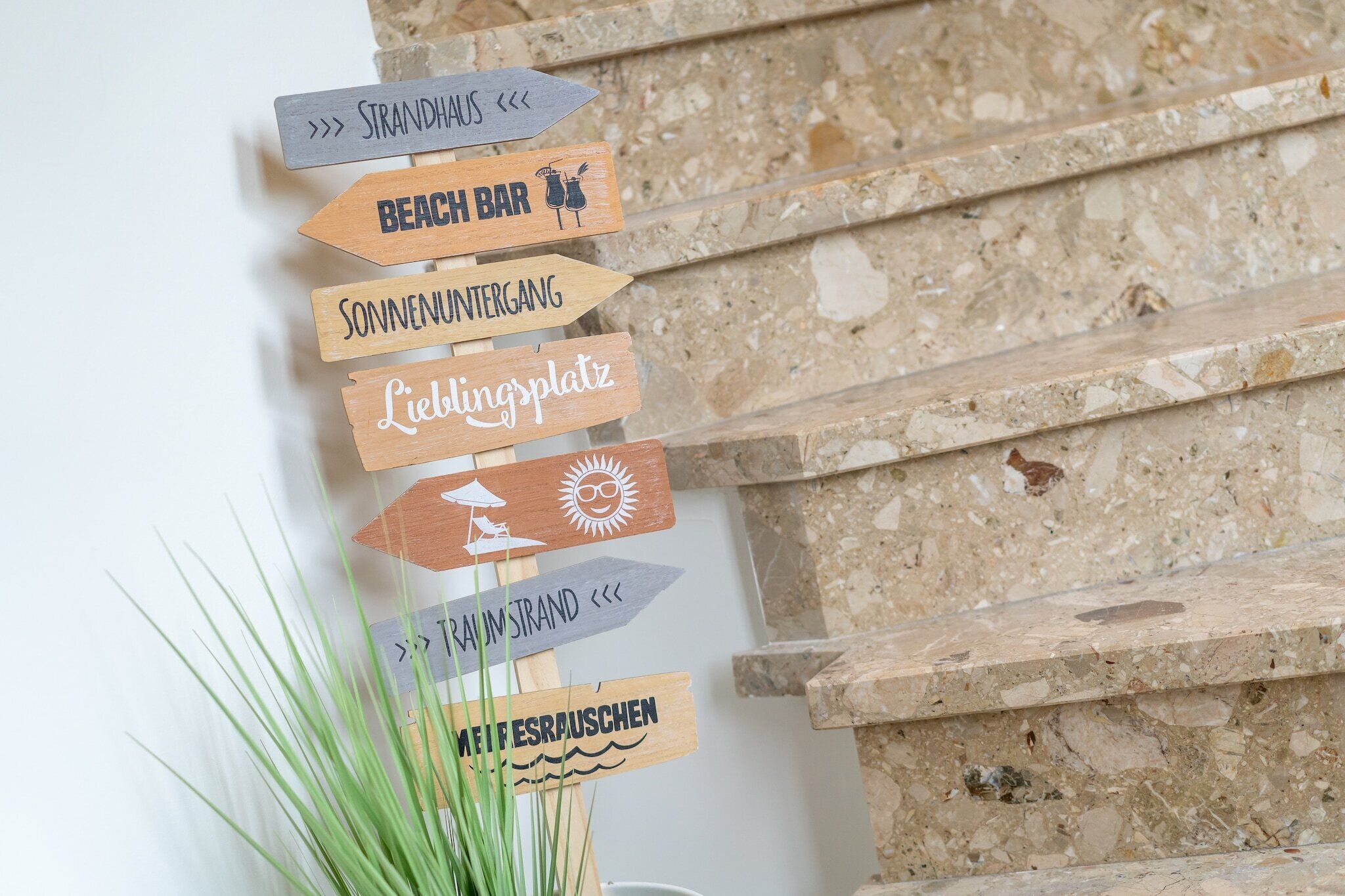 Wooden signs with various destinations like 'Beach Bar' and 'Lieblingplatz' against a stone wall.