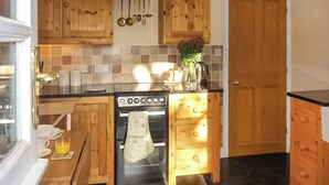 A kitchen with wooden cabinets, a stove, and a countertop with kitchen utensils hanging above.