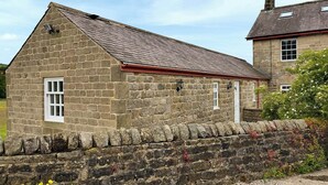 A stone building with a pitched roof, a small window, and a stone wall in front.