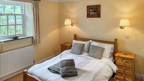 A neatly made bed with a wooden frame, two bedside tables, a window with curtains, and a wall-mounted picture.